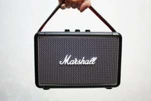 Close-up of a portable Bluetooth speaker held by a hand against a plain background.